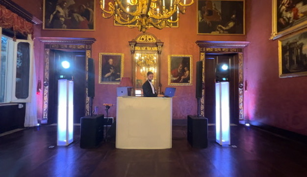 DJ booth in a red palazzo hall beneath a gilded chandelier