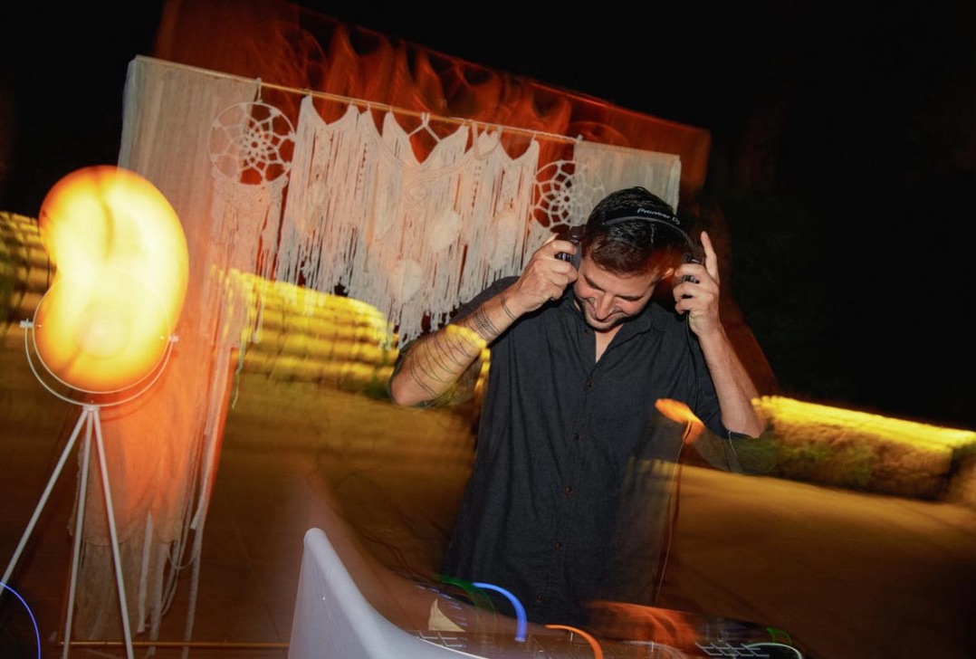 DJ cueing up behind a macrame backdrop at an outdoor party
