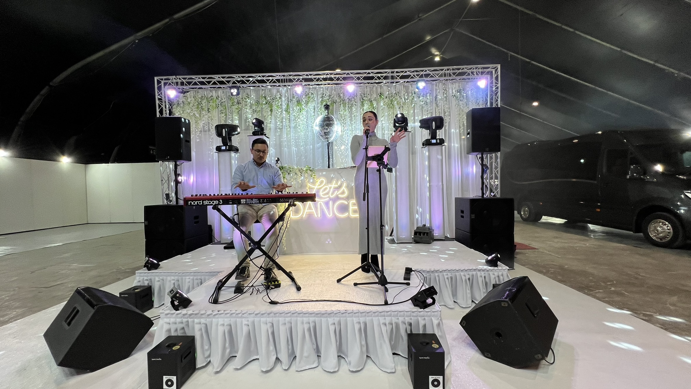 Singer and pianist on a white stage with truss lighting