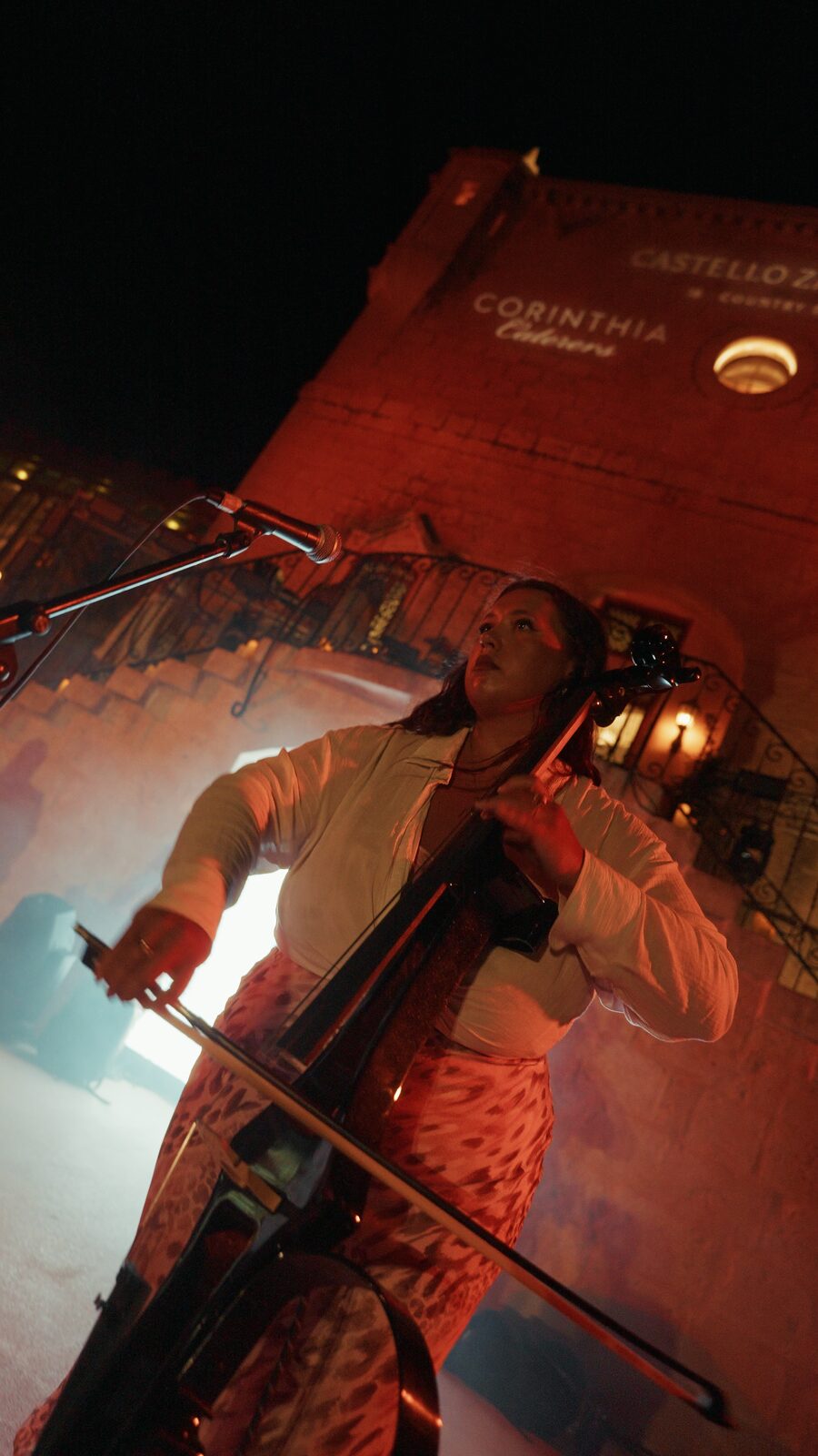 Cellist looking up mid performance against the castle wall