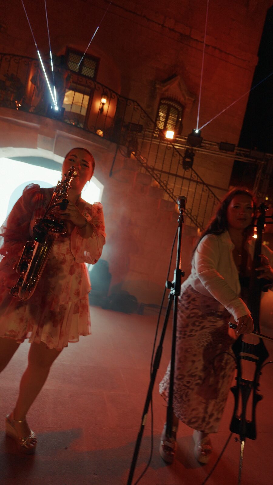 Saxophone and cello performing side by side in red stage light